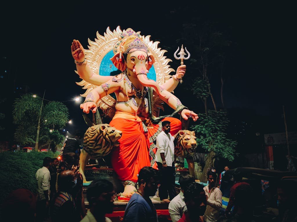 Joyful celebration of Ganesh Chaturthi with people gathering around a vibrant Ganesha idol at night.